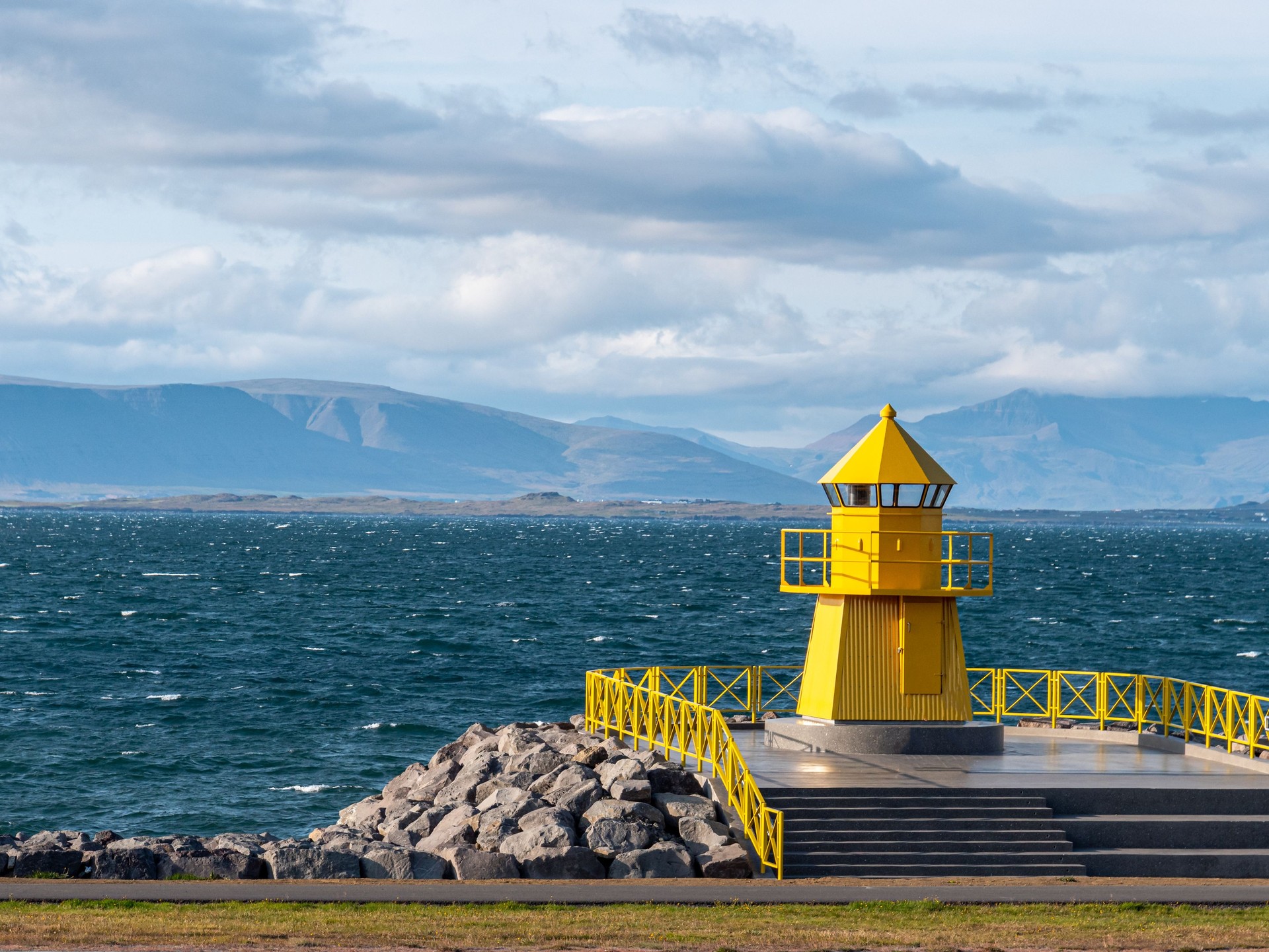 Yellow lighthouse tower on stone breakwater, entrance to Reykjavik port